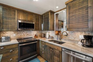 A kitchen with wooden cabinets, a stainless steel oven, a microwave, and a coffee maker. - Ma'alaea Surf #C-7 – Oceanfront Getaway with Spectacular Views & Pool (Kihei, Maui)