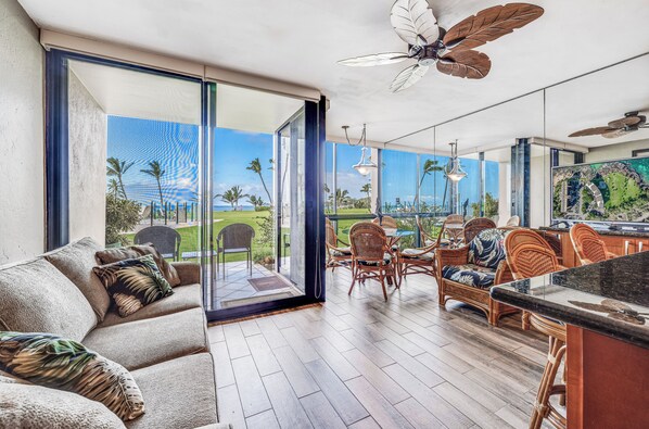 A spacious living area with a large sliding glass door leading to a balcony, wicker furniture, and a ceiling fan.