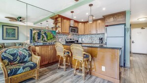 Una cocina con armarios de madera, una isla central con taburetes de bar, un microondas y un refrigerador.