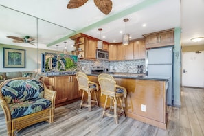 Una cocina con armarios de madera, una isla central con taburetes de bar, un microondas y un refrigerador.