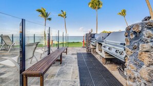 Un patio exterior con pared de piedra, una parrilla y un banco con vista al océano.