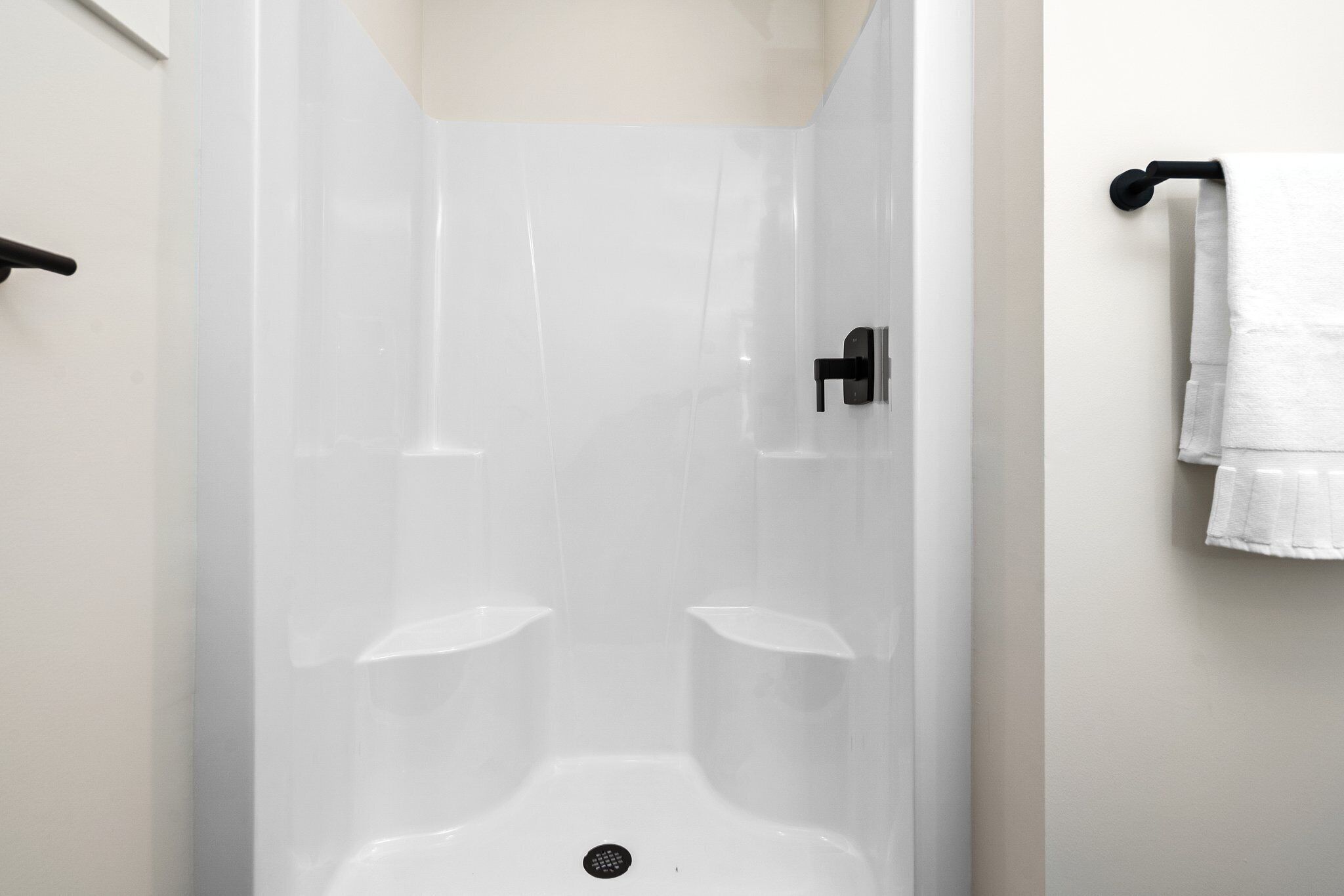 A shower with a glass door, a black faucet, and a white towel hanging on a hook.
