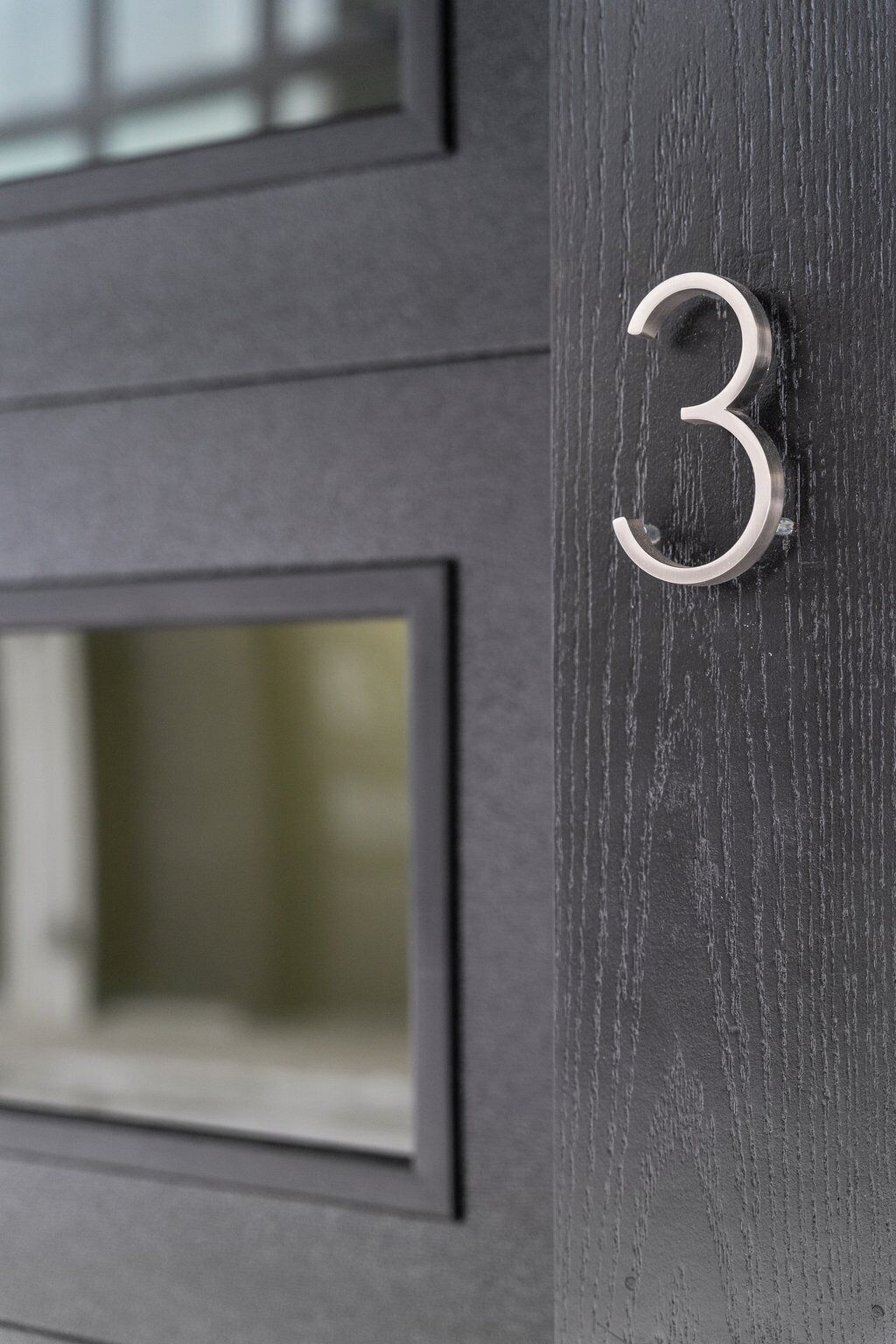 A dark wooden door with a metal number plate displaying the number 3.