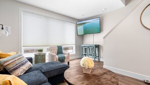 Uma sala de estar moderna com uma televisão grande, assentos confortáveis e vista para o exterior.