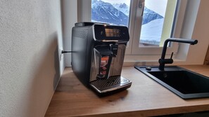 A coffee maker on a wooden countertop near a window with a view of snow-covered mountains.