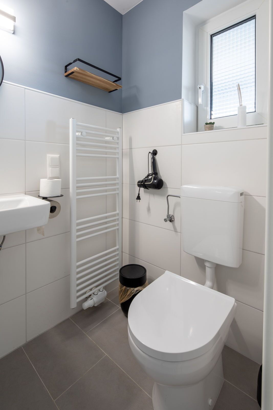 Un bagno con il water, un lavandino, un portasciugamani, un termosifone e una finestra.