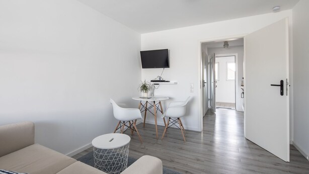 Ein modernes Wohnzimmer mit einer Couch, einem kleinen runden Tisch und einem an der Wand befestigten Fernseher.