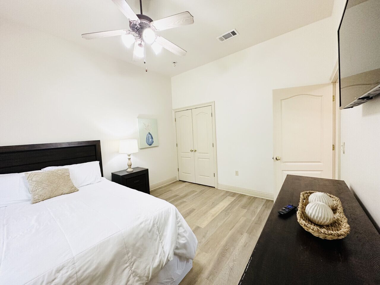 Quarto com cama, mesa de cabeceira e televisão fixada na parede.