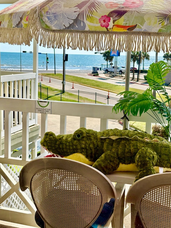 A balcony with a view of the ocean, a designated smoking area sign, and a large green stuffed crocodile.