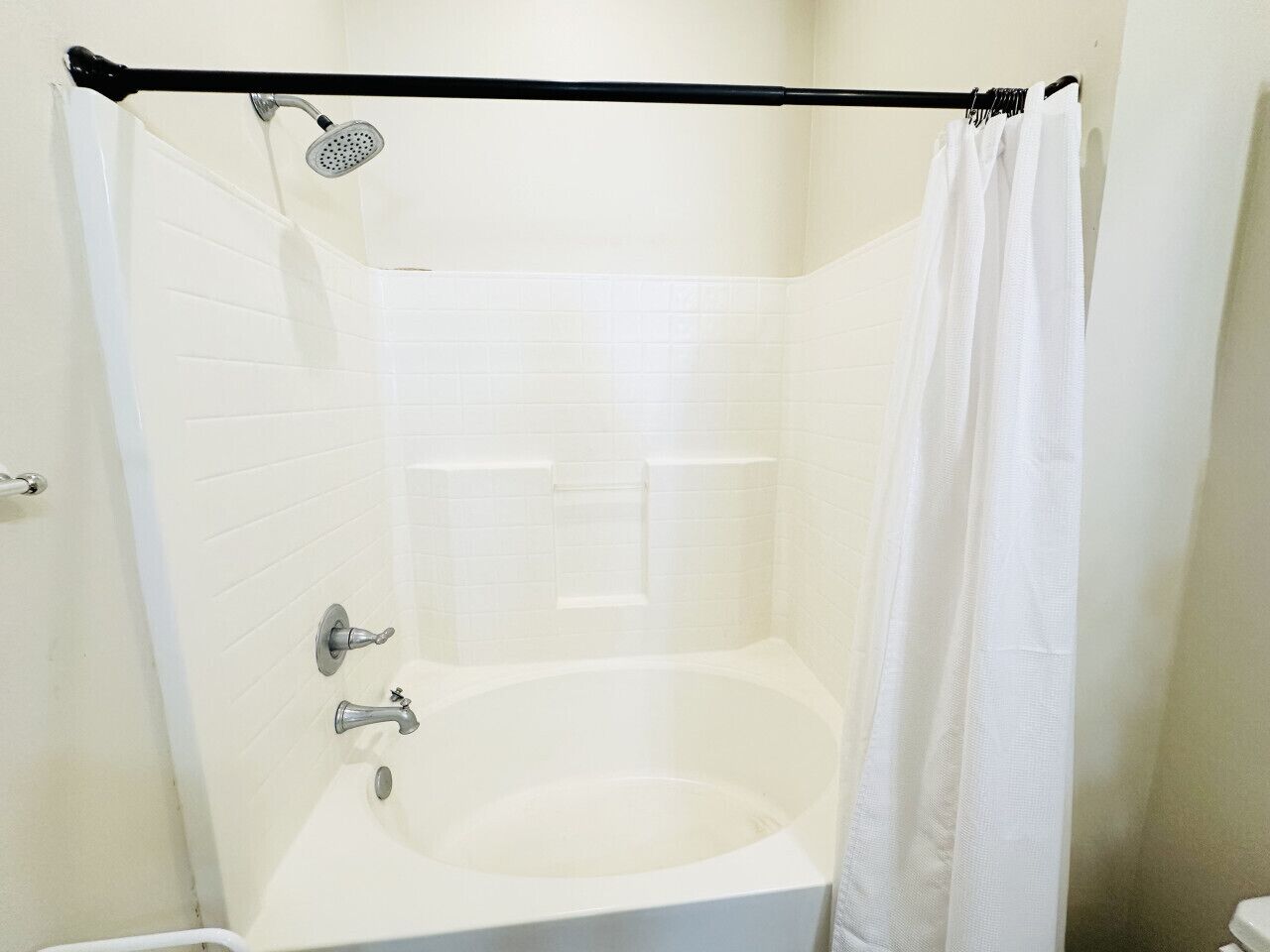 A white bathtub with a showerhead and curtain in a corner of a room with white tiled walls.