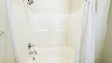 A white bathtub with a showerhead and curtain in a corner of a room with white tiled walls.