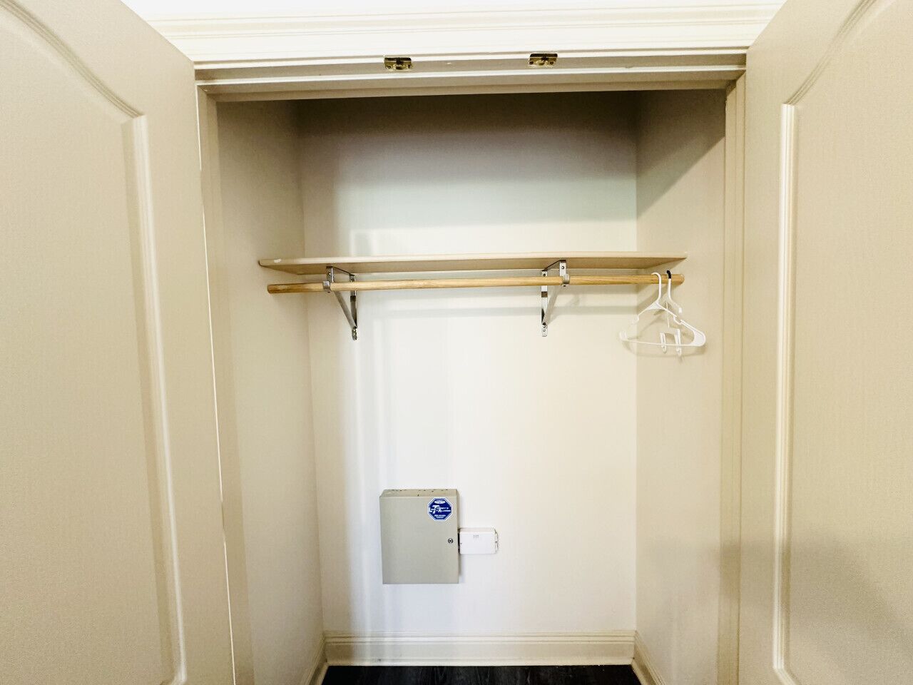 Un dressing avec une étagère en bois, une tringle et une prise de courant.