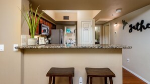 A kitchen with a granite countertop, two wooden stools, a potted plant, and a wall-mounted sign that reads "Penny." - 2 King Suites with Heated Pools/Spas/Gym in great North Scottsdale Location! (Scottsdale)