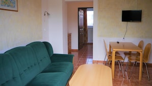 Ein Wohnzimmer mit einem grünen Sofa, einem Holztisch und einem Essbereich mit Tisch und Stühlen.