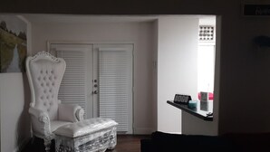 Ein Zimmer mit einem weiß gepolsterten Sessel, einem kleinen Tisch und einer weißen Tür mit Jalousien.