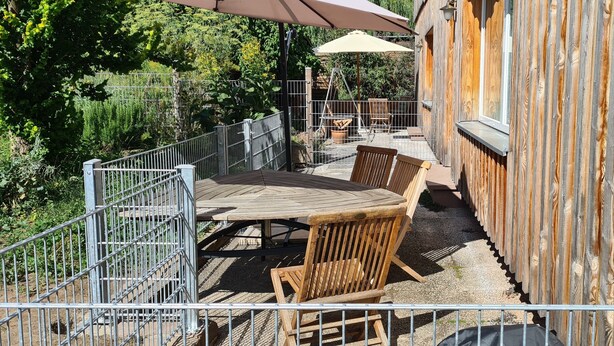 An outdoor patio with a wooden table and chairs, a metal railing, and a wooden fence. - 5-star vacation apartment "Hedfan" in Cnauceltaidd (Halle)