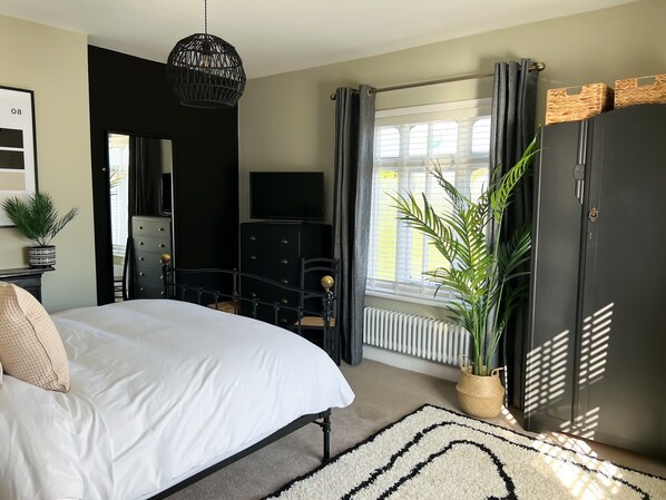 A bedroom with a bed, a television, a dresser, a radiator, and a window with curtains. - Idyllic Victorian Cottage Open Fire, Hot Tub, Sleeps 8, City 5 mins, Zoo 15 mins (Chester)