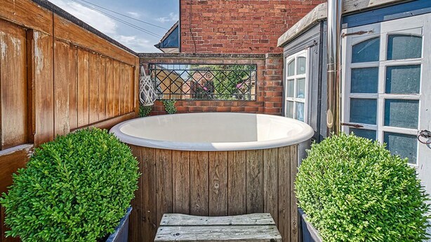 A wooden deck with a hot tub, surrounded by brick walls and a window.