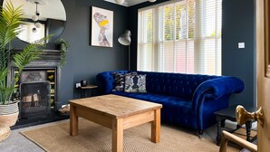 A living room with a blue sofa, a wooden coffee table, a fireplace, and a large window with blinds.
