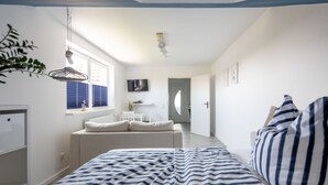 Ein Schlafzimmer mit einem Bett, einem Schreibtisch, einem Stuhl, einem Fernseher und einem Fenster mit Jalousien.