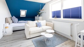 Ein modernes Schlafzimmer mit blauer Akzentwand, einem Bett mit gestreifter Bettwäsche, einem weißen Sofa und einem Fenster mit blauen Jalousien.