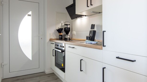 Eine moderne Küche mit weißen Schränken, einer Holz Arbeitsplatte, einem eingebauten Ofen und einer schwarzen Dunstabzugshaube.