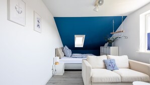Ein modernes Schlafzimmer im Loft-Stil mit Schrägwand, Dachfenster, einer weißen Couch, einem Bett mit gestreiften Kissen und einem kleinen Tisch.