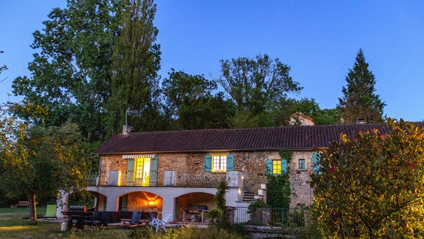 Una casa de piedra con techo de tejas, varias ventanas y un balcón.