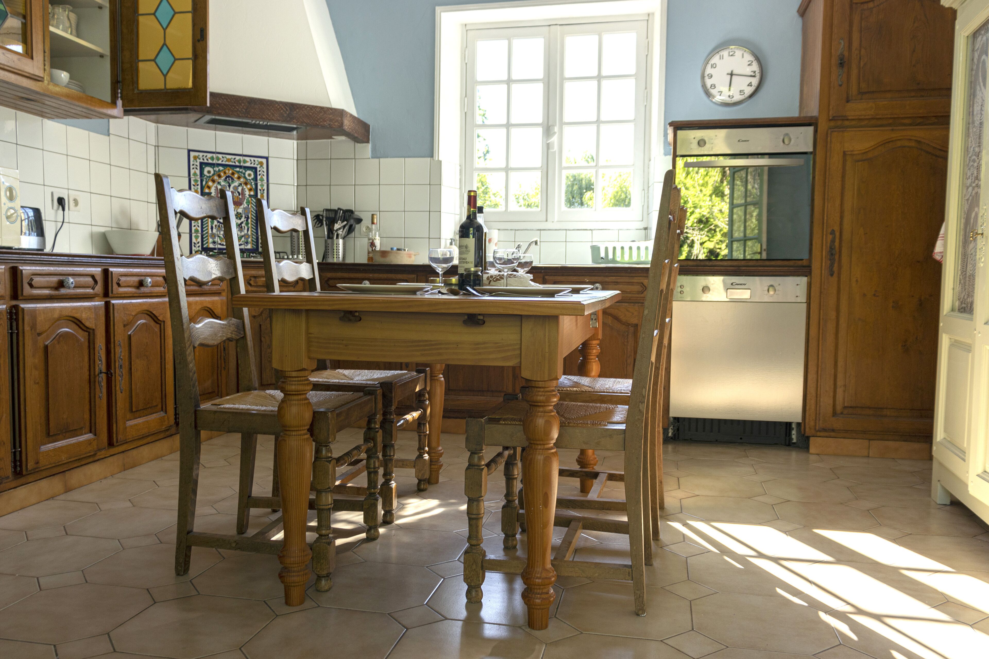Een keuken met een houten kookeiland, stoelen, een klok en een raam.