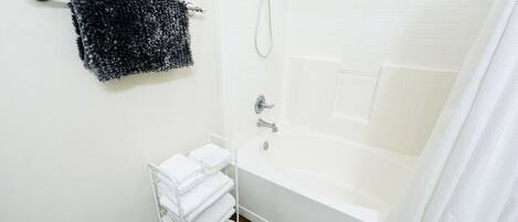 Ett badrum med ett badkar, en dusch, en handdukshängare med en svart handduk och en vit handdukshängare med flera vita handdukar.