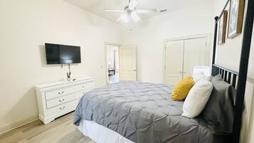 A bedroom with a bed, a dresser, a ceiling fan, and a TV.