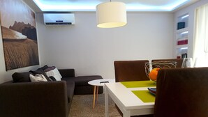 Un salon moderne comprenant un canapé, une table à manger avec des chaises, une lampe suspendue et un climatiseur fixé au mur.