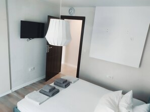 Ein modernes Schlafzimmer mit einem Bett, einem Flachbildfernseher, einer weißen Wanduhr und einer Tür zu einem anderen Raum.