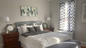 A bedroom with a bed, nightstands, a bench, a radiator, and a window with curtains. - Spectacular Location: State Circle Apartment (Annapolis)
