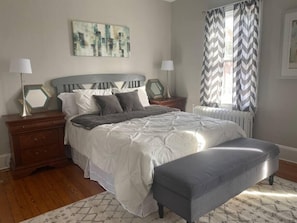 A bedroom with a bed, nightstands, a bench, a radiator, and a window with curtains. - Spectacular Location: State Circle Apartment (Annapolis)