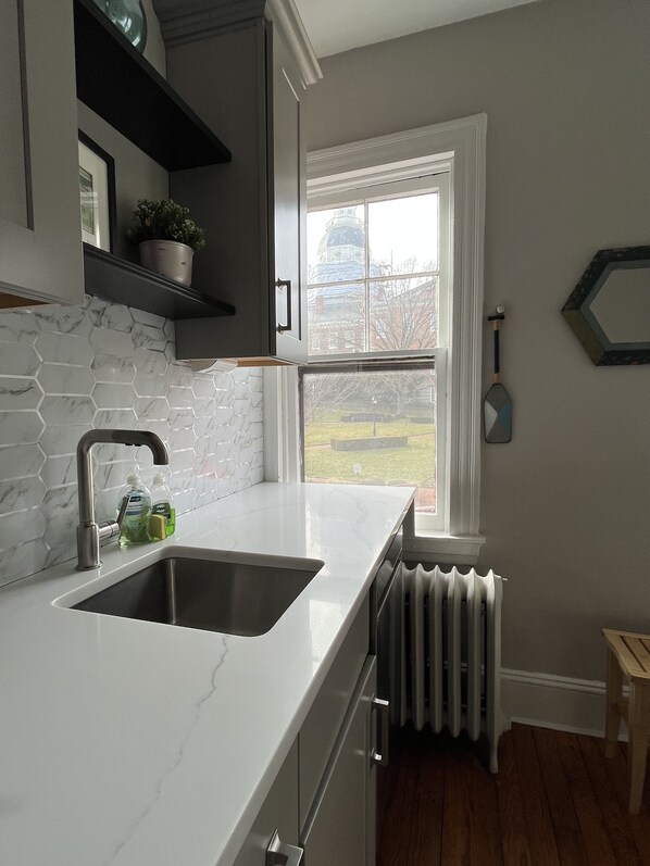 A kitchen with a double sink, white marble backsplash, and a window overlooking a garden. - Spectacular Location: State Circle Apartment (Annapolis)