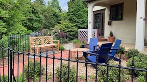 A patio with a wooden bench and blue chairs, a brick pathway, and a white building with a black door. - Spectacular Location: State Circle Apartment (Annapolis)