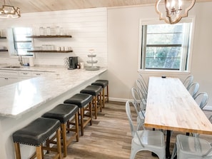 Une cuisine moderne dotée d’un plan de travail en marbre, de tabourets en bois et d’une table à manger en bois avec des chaises en métal.