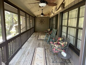 A covered porch with wooden flooring, a ceiling fan, and a row of chairs with floral cushions.