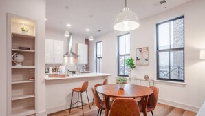 Een moderne keuken met witte kastjes, een centraal eiland en hangende lampen. Twee ramen zorgen voor natuurlijk licht en uitzicht.