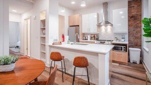 Een moderne keuken met witte kasten, een roestvrijstalen afzuigkap en een ingebouwde magnetron. Er staat een houten eettafel met twee stoelen en een bloempot.
