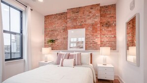 Een slaapkamer met een bakstenen muur, een groot bed, nachtkastjes met lampen en een raam.