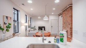 Een moderne keuken met een centraal eiland, een eethoek met een houten tafel en een bakstenen muur.