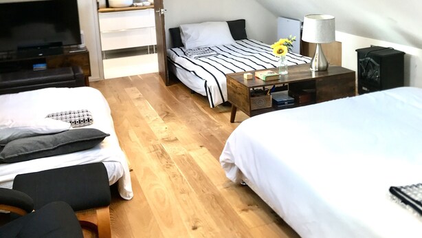 A modern, well-lit attic bedroom with a sloped ceiling, wooden flooring, and a skylight. There are two beds, a desk, and a TV. - Cosy new Loft with bathroom and facilities (Glynneath)
