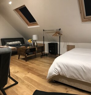 A bedroom with a bed, a desk, a chair, a small table with a lamp, a window, and a fireplace. - Cosy new Loft with bathroom and facilities (Glynneath)