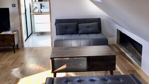 A modern loft bedroom with a sloped ceiling, a dark grey sofa, a wooden coffee table, and a black leather ottoman. - Cosy new Loft with bathroom and facilities (Glynneath)
