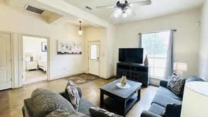 A spacious living room with a flat-screen TV, a ceiling fan, and a large window. - Chateau 7, spacious townhouse in Tickfaw, LA (Tickfaw)