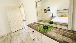 A bedroom with a large mirror, a bed with a white comforter, a nightstand with a lamp, and a dresser with drawers. - Chateau 7, spacious townhouse in Tickfaw, LA (Tickfaw)
