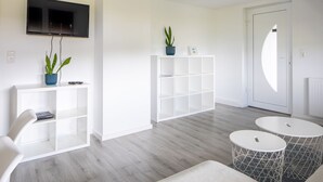 A modern living room with a flat-screen TV, white shelving units, a potted plant, and two round tables.