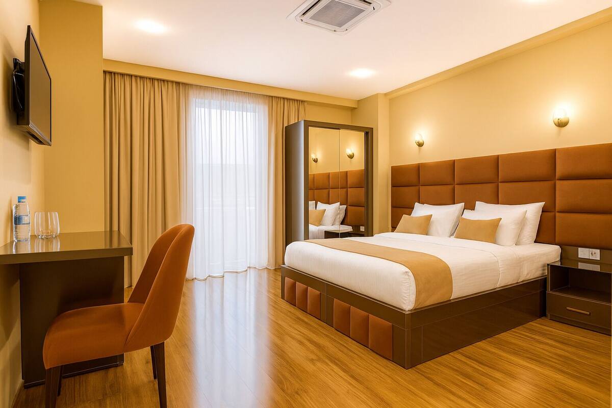 Una habitación de hotel con cama, escritorio, silla, televisor y un espejo grande.